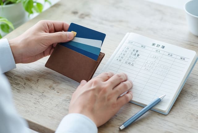財布とレシートを前に家計簿をつける手元